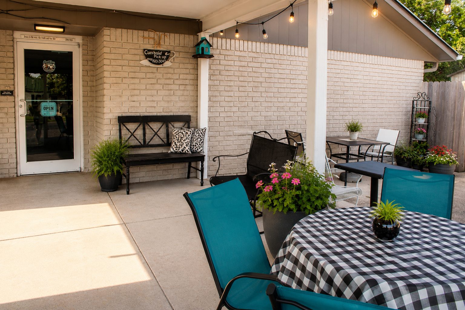 Covered patio beside the entrance with curbside pickup sign, bench and flowers